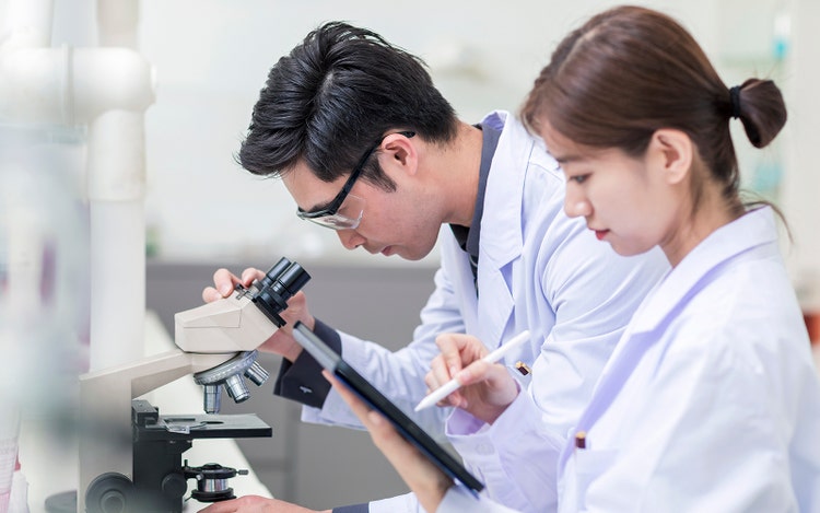 Close up of Young scientist looking through a microscope in a laboratory.